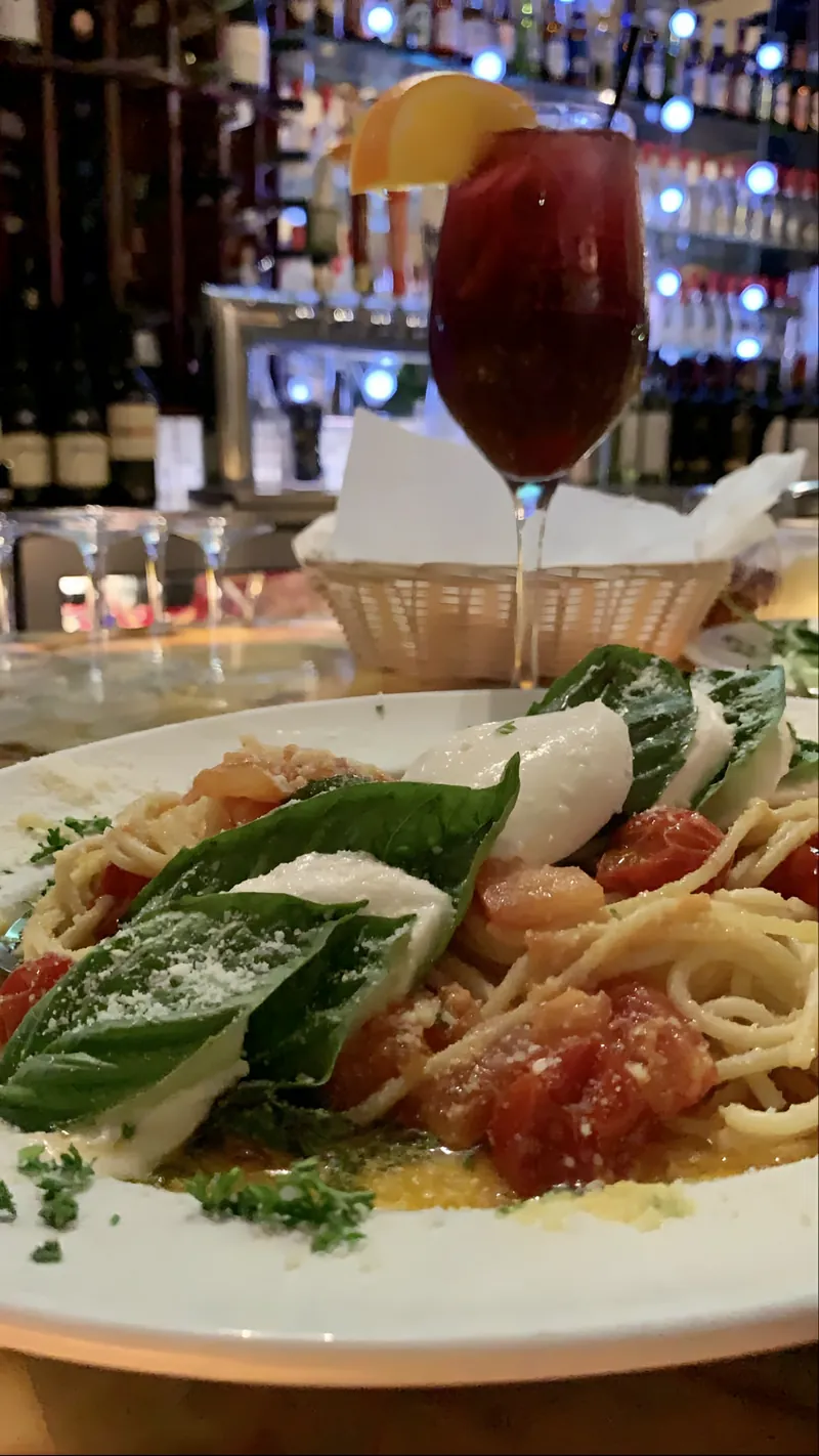 Spaghetti with tomatoes, fresh mozzarella and basil at the bar, a glass of sangria behind it