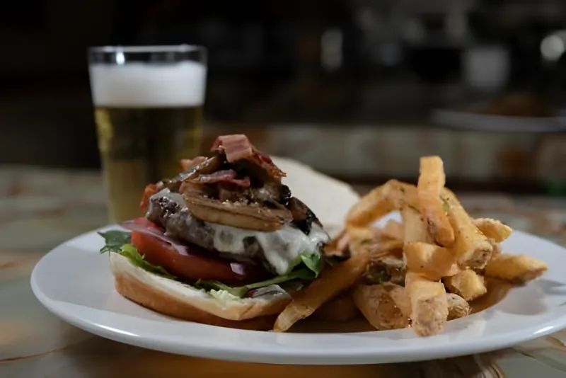 A mushroom and bacon burger with fries and a cold beer