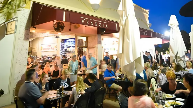 Venezia at night on St. Armands Circle, every sidewalk table full under the crimson awning